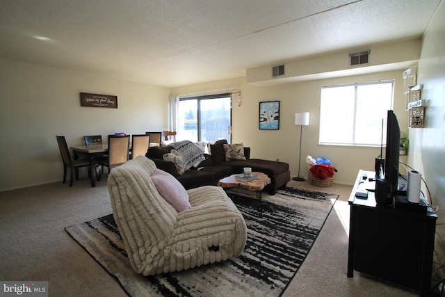 carpeted living area featuring visible vents, a textured ceiling, and baseboards