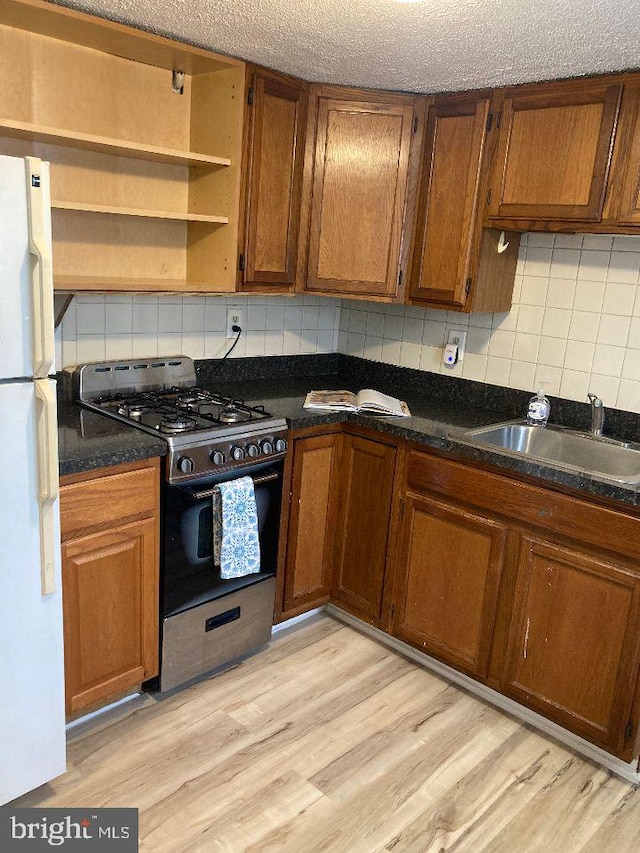 kitchen featuring brown cabinets, freestanding refrigerator, light wood-style floors, a sink, and gas stove