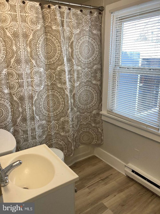 full bathroom with toilet, a sink, baseboard heating, and wood finished floors