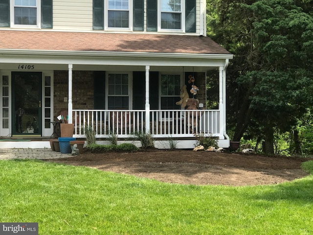 entrance to property featuring a porch, roof with shingles, and a lawn