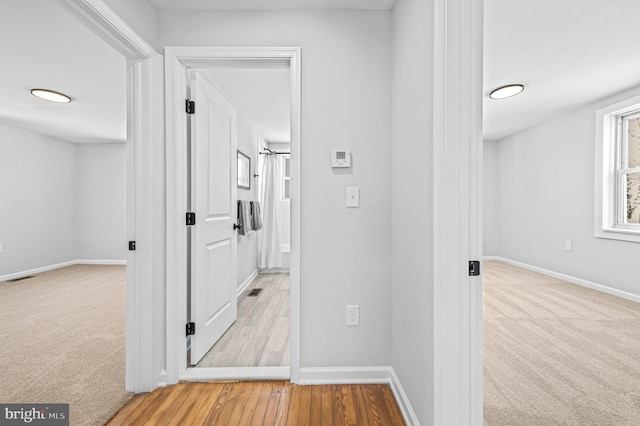 corridor featuring visible vents, baseboards, and light colored carpet