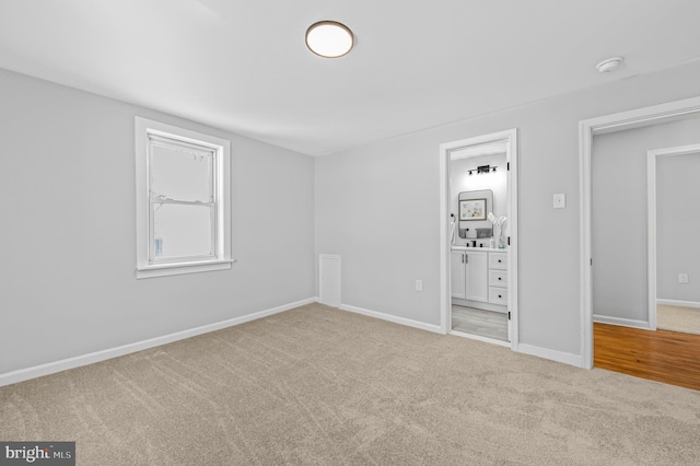 unfurnished bedroom with ensuite bath, baseboards, and light colored carpet