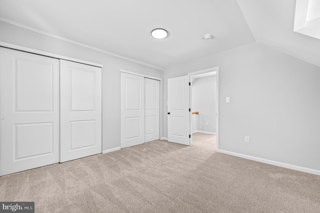 unfurnished bedroom featuring baseboards, vaulted ceiling, two closets, and light colored carpet