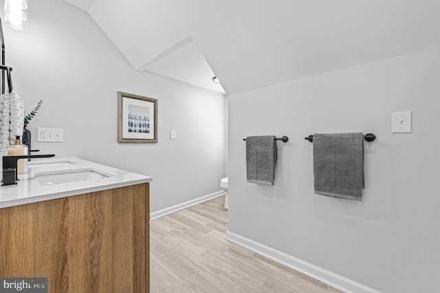 bathroom featuring double vanity, vaulted ceiling, a sink, wood finished floors, and baseboards