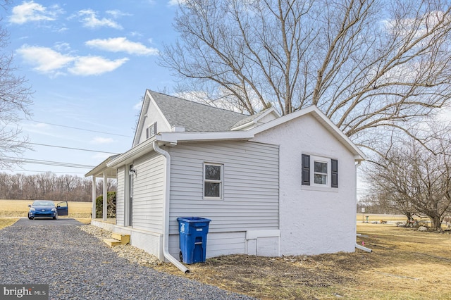 view of side of home with a shingled roof and gravel driveway