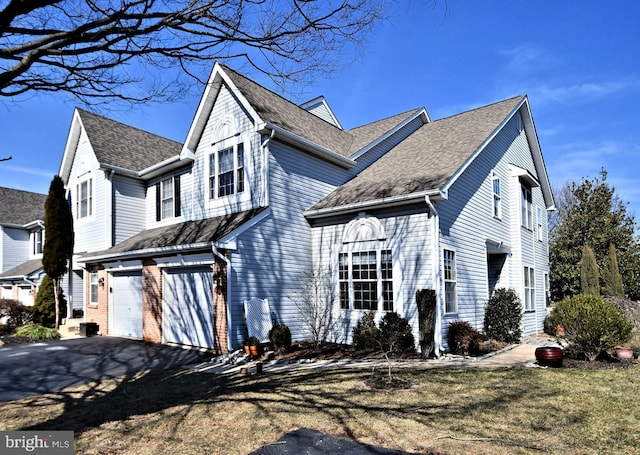 traditional home featuring a garage, roof with shingles, aphalt driveway, and brick siding