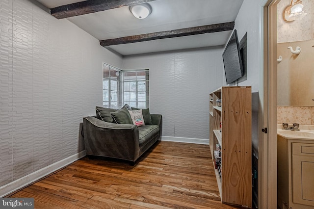 sitting room with a textured wall, baseboards, beam ceiling, and wood finished floors