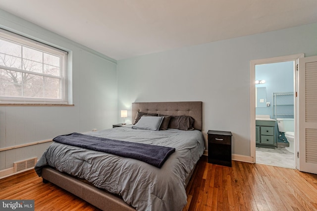 bedroom with ensuite bath, wood-type flooring, visible vents, and baseboards