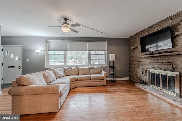 living room featuring a ceiling fan, a stone fireplace, and light wood finished floors