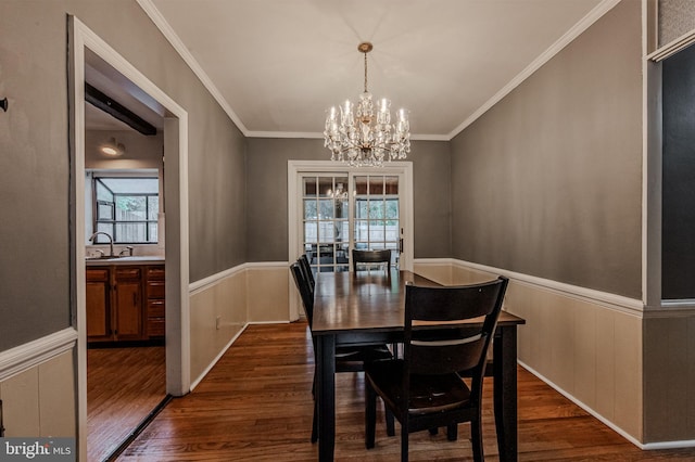 dining area featuring dark wood-style floors, wainscoting, crown molding, and an inviting chandelier