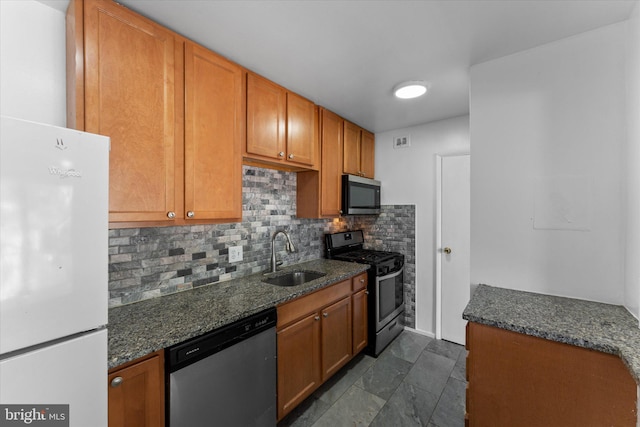 kitchen with stainless steel appliances, a sink, tasteful backsplash, brown cabinetry, and dark stone countertops