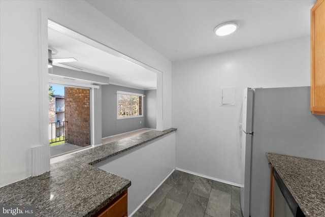 kitchen with a ceiling fan, freestanding refrigerator, baseboards, and dark stone countertops