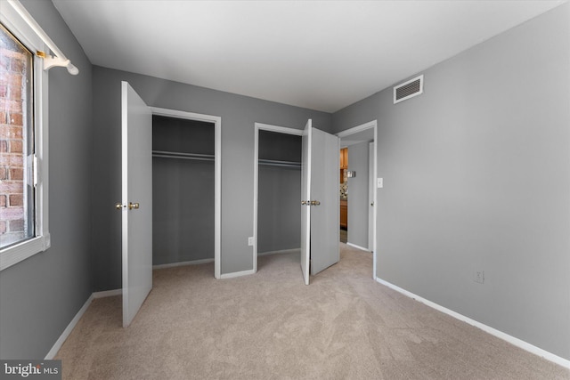 unfurnished bedroom featuring multiple closets, visible vents, light carpet, and baseboards