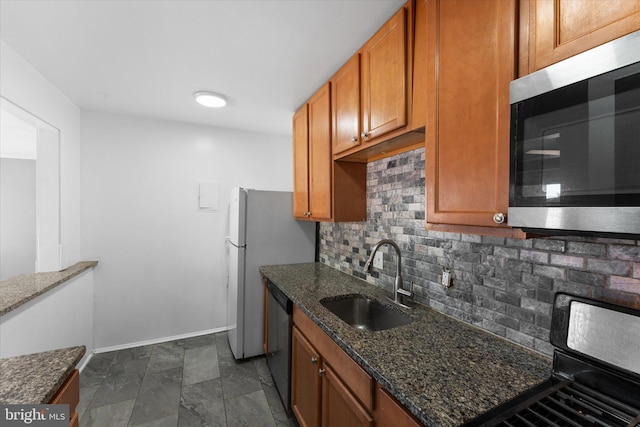 kitchen with tasteful backsplash, appliances with stainless steel finishes, a sink, dark stone countertops, and baseboards