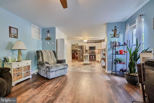 living area featuring baseboards, ceiling fan, visible vents, and wood finished floors