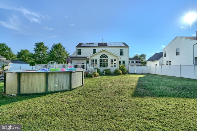 rear view of house with a yard, solar panels, a fenced backyard, and a fenced in pool