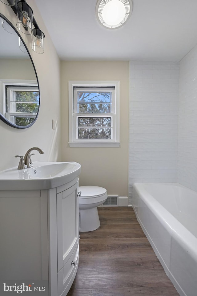 full bathroom with toilet, visible vents, a wealth of natural light, and wood finished floors