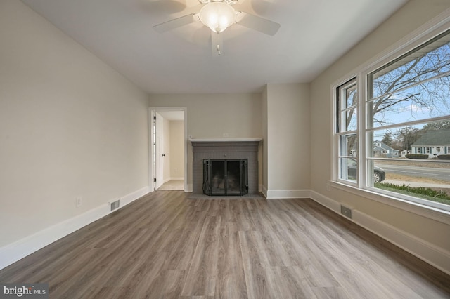 unfurnished living room with a brick fireplace, wood finished floors, visible vents, and baseboards