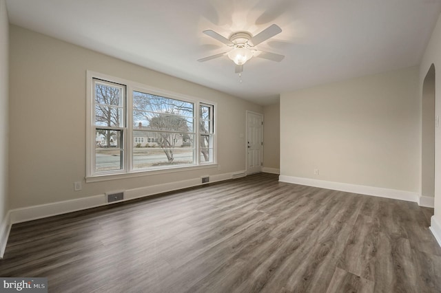 unfurnished room featuring arched walkways, wood finished floors, visible vents, and baseboards