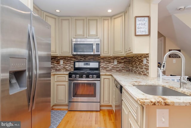 kitchen with stainless steel appliances, a sink, light stone counters, and cream cabinets