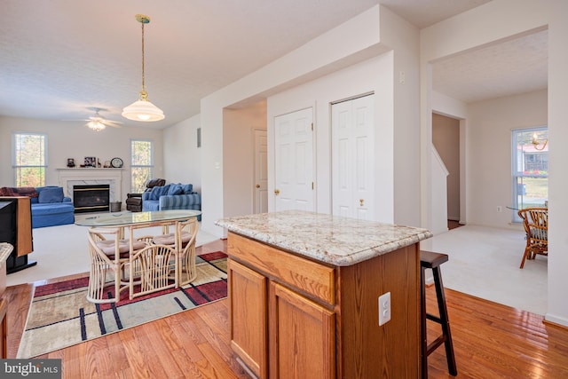 kitchen with pendant lighting, a breakfast bar area, light wood finished floors, a premium fireplace, and a kitchen island