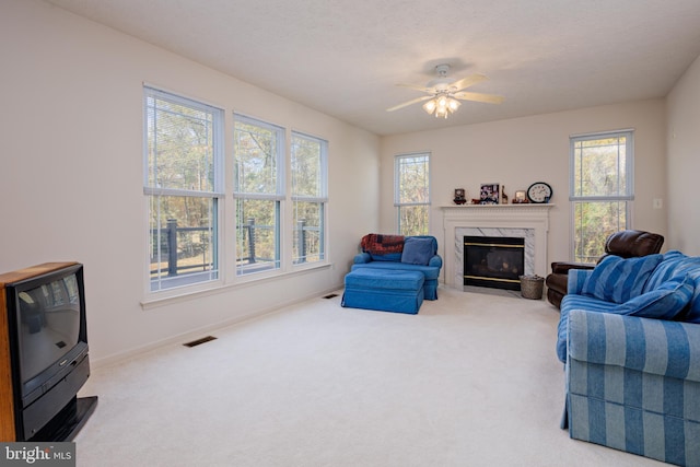 carpeted living area with a ceiling fan, visible vents, baseboards, and a premium fireplace