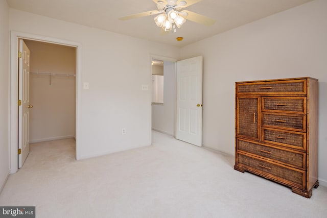 unfurnished bedroom with a ceiling fan, light colored carpet, a spacious closet, and baseboards