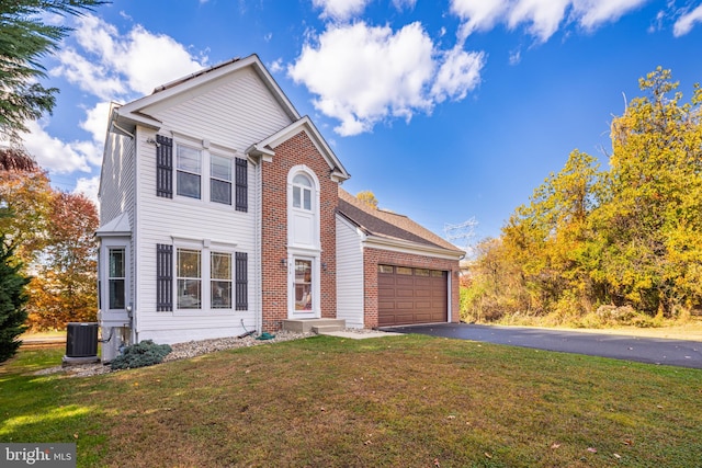 traditional-style home with driveway, brick siding, an attached garage, central air condition unit, and a front yard