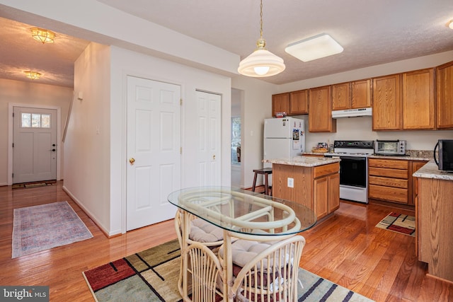 kitchen featuring a center island, brown cabinetry, wood finished floors, white appliances, and under cabinet range hood