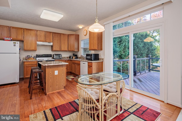 kitchen with brown cabinets, light wood-style flooring, a kitchen island, white appliances, and under cabinet range hood