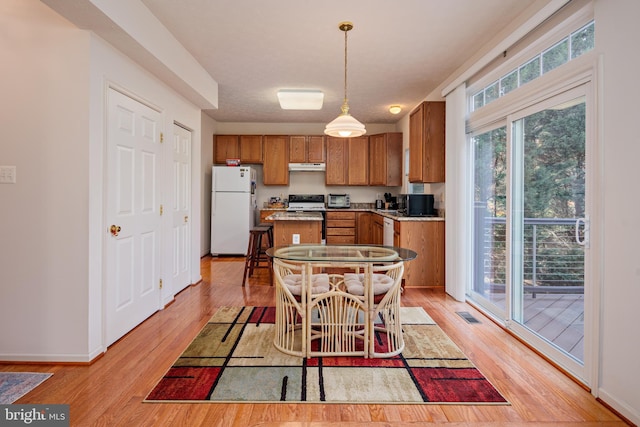 kitchen with white appliances, brown cabinets, a center island, decorative light fixtures, and under cabinet range hood