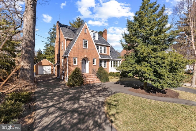 view of front facade featuring brick siding, a detached garage, a chimney, an outdoor structure, and driveway