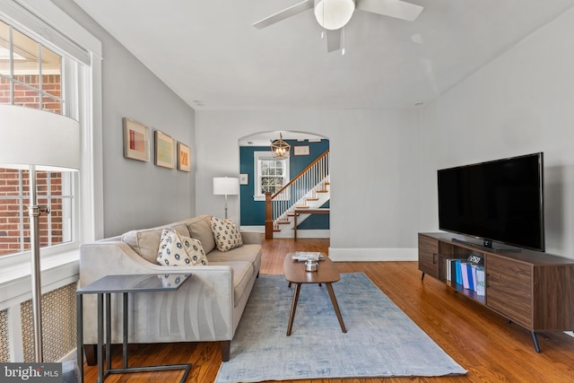 living area featuring baseboards, arched walkways, ceiling fan, wood finished floors, and stairs