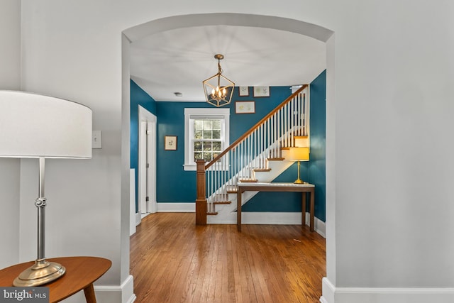 entryway featuring baseboards, arched walkways, hardwood / wood-style floors, stairs, and a chandelier