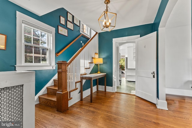 entrance foyer with arched walkways, wood finished floors, a healthy amount of sunlight, stairs, and baseboards