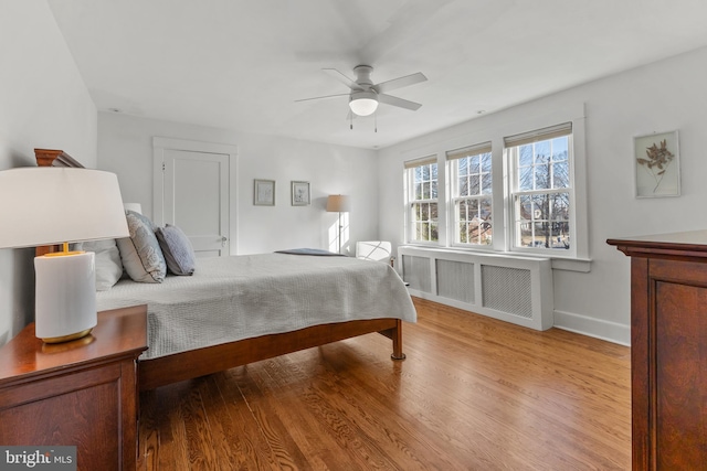 bedroom with light wood-style floors, baseboards, radiator heating unit, and a ceiling fan