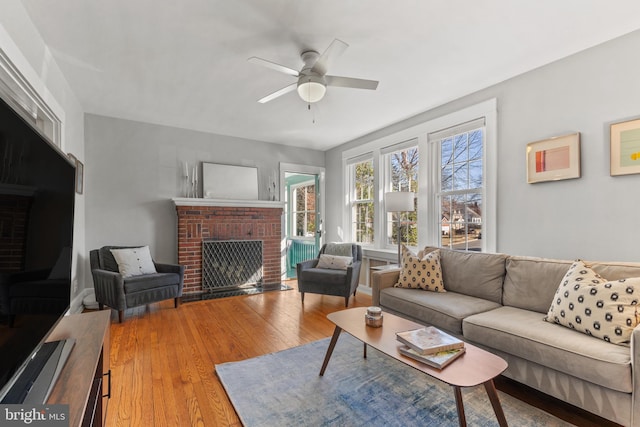 living area with a ceiling fan, a brick fireplace, and wood finished floors