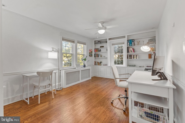 office space with built in features, ceiling fan, radiator heating unit, and wood finished floors