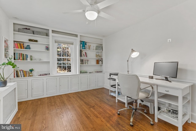 office space with a ceiling fan, built in shelves, and wood finished floors