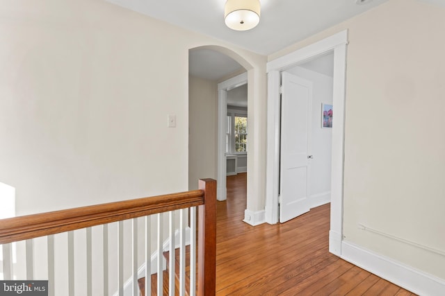 hall with hardwood / wood-style flooring, baseboards, and arched walkways