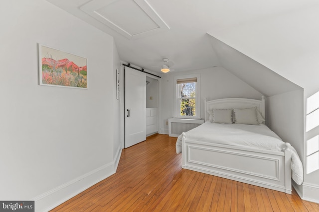 bedroom featuring attic access, a barn door, lofted ceiling, radiator heating unit, and light wood-style floors