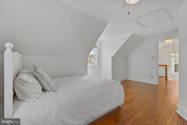 bedroom with ceiling fan, baseboards, vaulted ceiling, wood-type flooring, and attic access