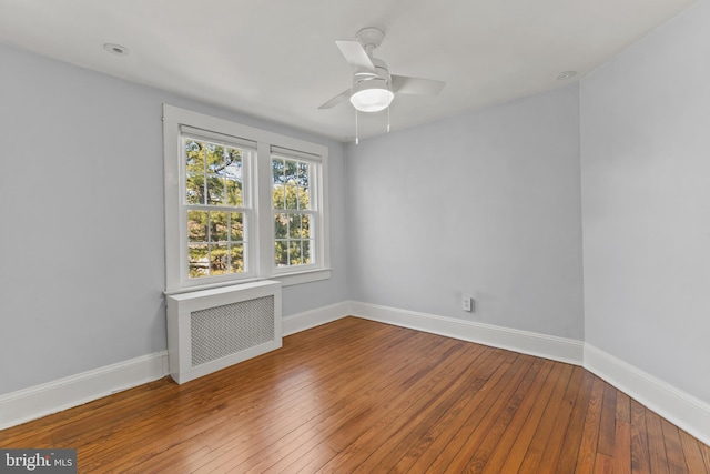 spare room with a ceiling fan, radiator, baseboards, and hardwood / wood-style floors