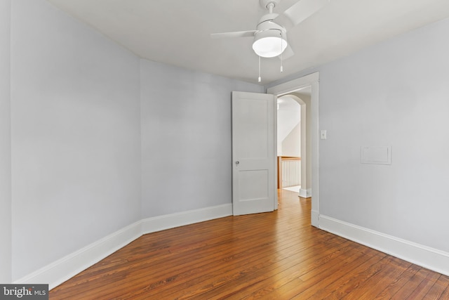 empty room with arched walkways, hardwood / wood-style floors, a ceiling fan, and baseboards