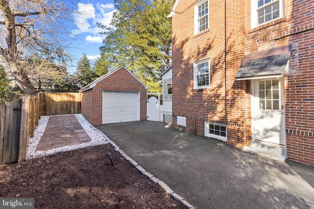 view of side of property featuring brick siding, aphalt driveway, a detached garage, and an outdoor structure