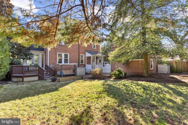 view of front of property featuring brick siding, a wooden deck, a gate, fence, and a front lawn