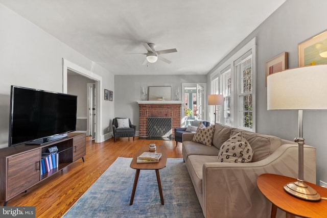 living area with a fireplace, ceiling fan, baseboards, and wood finished floors