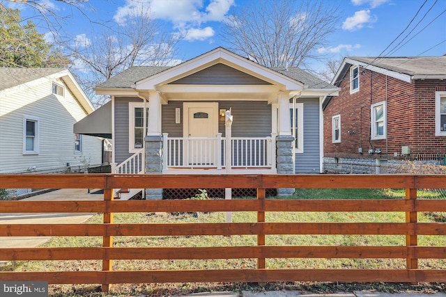 bungalow-style house with a fenced front yard, a porch, and a shingled roof