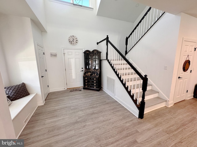 entryway with a towering ceiling, visible vents, stairway, and wood finished floors