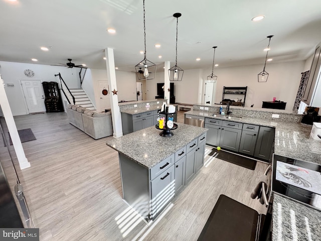 kitchen featuring gray cabinetry, a kitchen island, a sink, open floor plan, and light wood finished floors